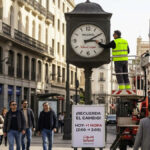 فني يقوم بتقديم عقارب الساعة في مدريد معلناً بدء التوقيت الصيفي في إسبانيا، وشعار صوت إسبانيا يظهر على الساعة