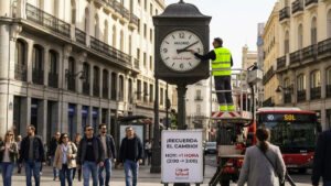 فني يقوم بتقديم عقارب الساعة في مدريد معلناً بدء التوقيت الصيفي في إسبانيا، وشعار صوت إسبانيا يظهر على الساعة