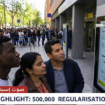 A diverse group of undocumented immigrants waits inside the Madrid Immigration Office ('Oficina de Extranjería') to submit paperwork for Spain's 2026 massive regularisation process of 500,000 people. A large sign in Spanish details the requirements and deadlines, while an official with a HIGRH NEWS vest assists a hopeful couple, highlighting the start of the historic event.